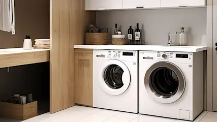 Buanderie avec deux machines à laver blanches sous une étagère contenant des bouteilles et des paniers, un lavabo en bois.