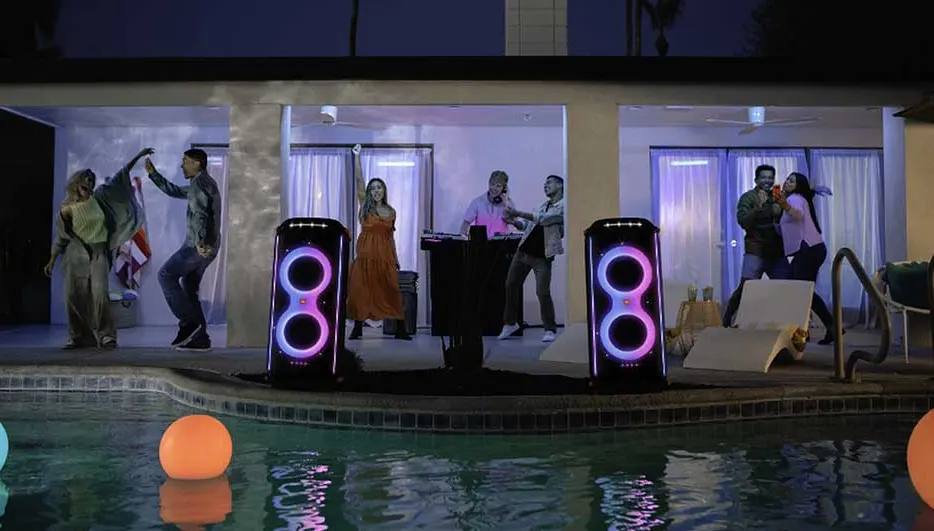 Fête nocturne au bord de la piscine avec lumières néon, haut-parleurs éclairés, eau reflétant la lumière et boules flottantes colorées.