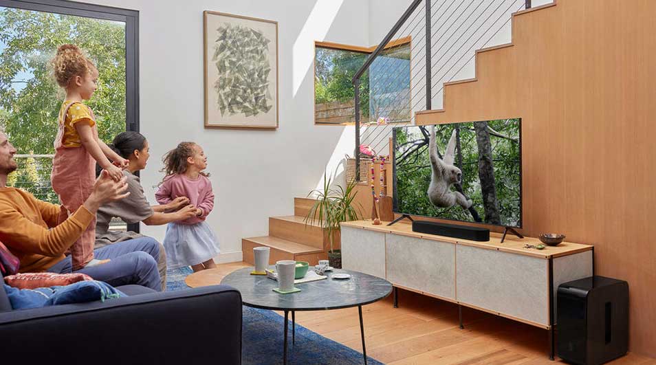 Une famille joyeuse regarde un programme animalier à la télévision dans un salon lumineux avec escalier en bois et déco moderne.