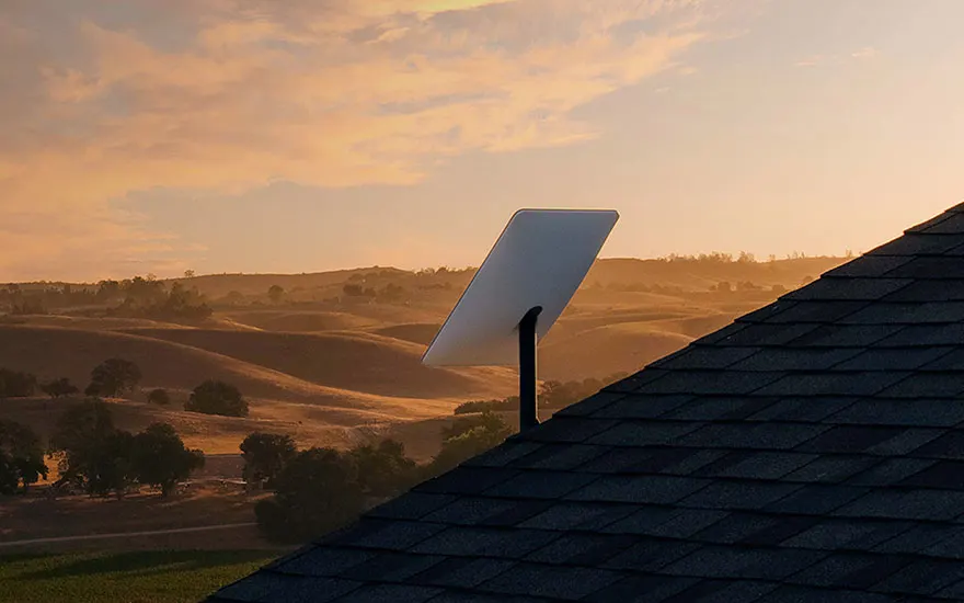 Un toit en ardoise avec une antenne parabolique rectangulaire. Arrière-plan de collines sous un ciel nuageux au coucher du soleil.