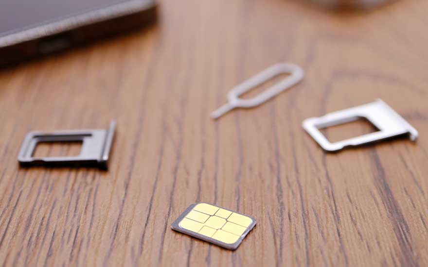 Sur une table en bois, une carte SIM jaune, un outil d'éjection et deux supports de carte SIM en métal.