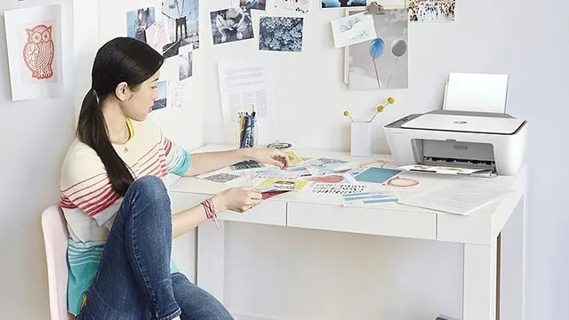 Une imprimante blanche sur un bureau blanc avec des papiers colorés. Un mur blanc décoré de photos.