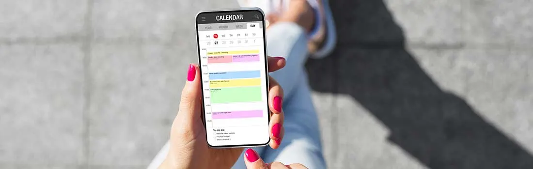 Un téléphone affiche un calendrier coloré sur un fond gris, mettant en évidence des rendez-vous.