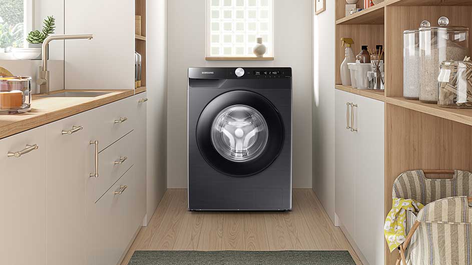 Een donkergrijze Samsung wasmachine staat in een wasruimte met witte kasten en houten vloeren.