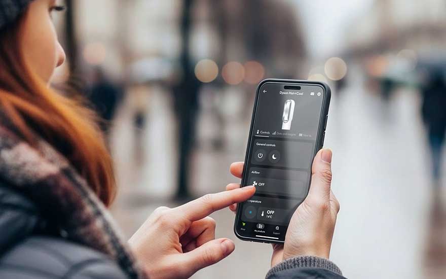 Buiten bedient een vrouw via haar smartphone een Dyson Hot+Cool-toestel, met een donkere interface en een onscherpe straat erachter.