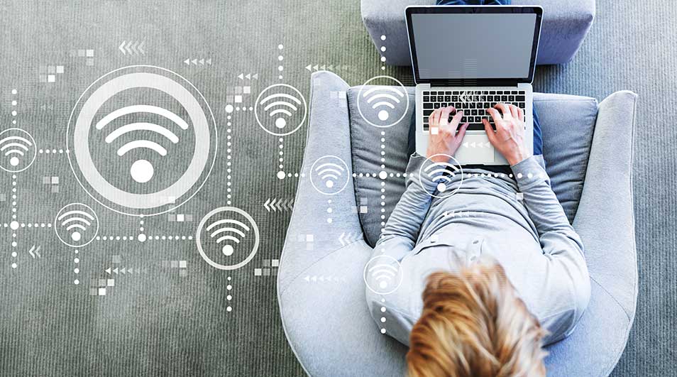 Une personne assise dans un fauteuil gris utilise un ordinateur portable, avec des symboles WiFi autour.