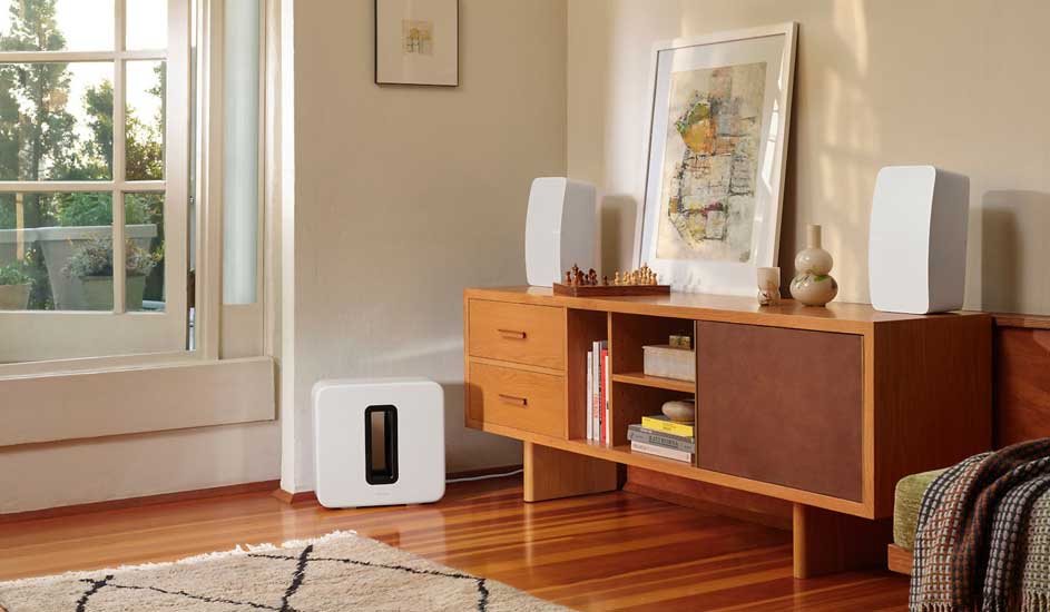 Een woonkamer met een houten vloer, een open raam en een lage kast met audioapparatuur erop.