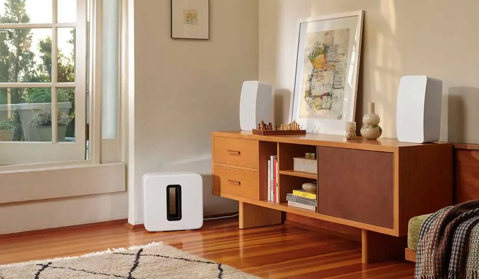 Een woonkamer met een houten vloer, een open raam en een lage kast met audioapparatuur erop.