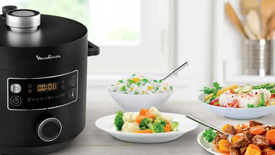 Cuisinier noir "Moulinex" avec repas variés: riz, légumes, poisson et ragoût. Vaisselle blanche, cuisine claire en arrière-plan.