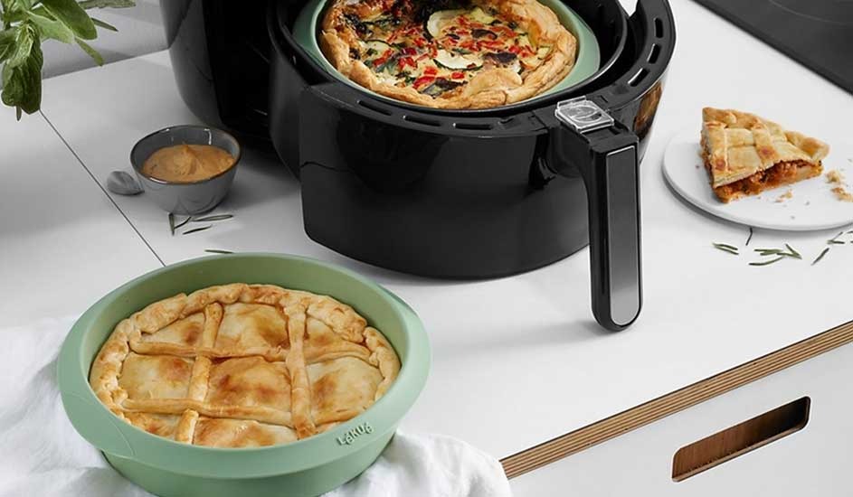 Two golden-brown pies sit on the worktop, one in an air fryer and one in a green dish, with a sliced piece set beside them.
