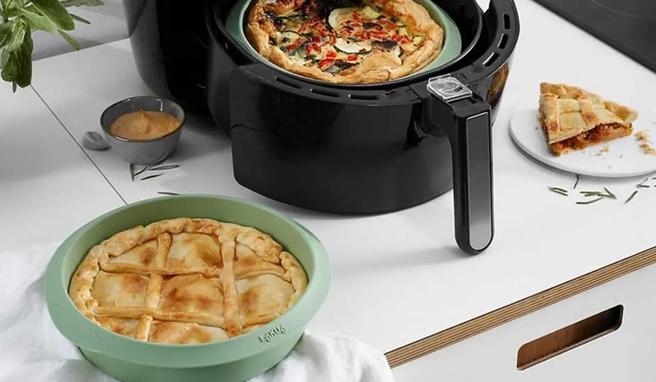 Two golden-brown pies sit on the worktop, one in an air fryer and one in a green dish, with a sliced piece set beside them.