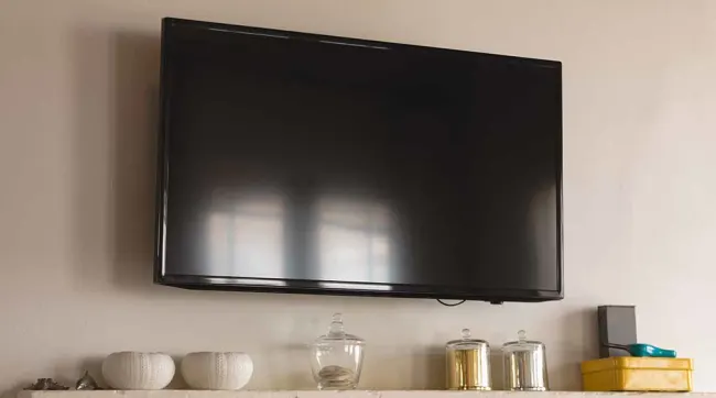 Een zwarte televisie hangt aan een muur boven een plank met decoratieve objecten.