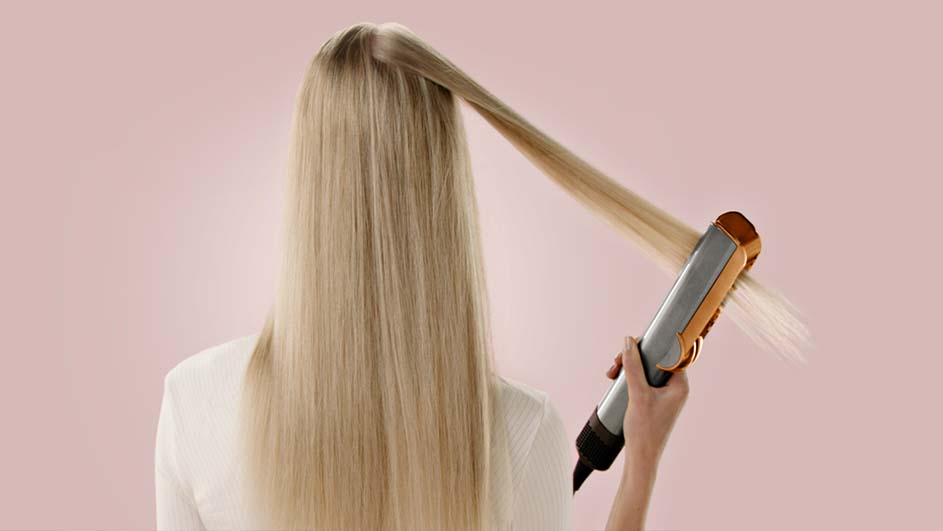 Vue arrière de cheveux blonds lisses coiffés avec un fer à lisser gris et orange sur un fond rose pâle.