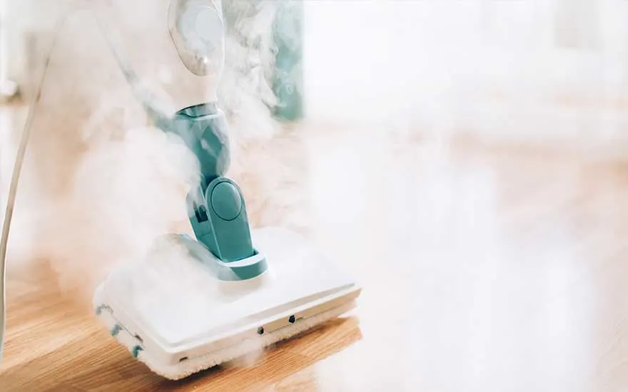 Een stoomreiniger met blauw handvat reinigt een houten vloer, omgeven door stoom.
