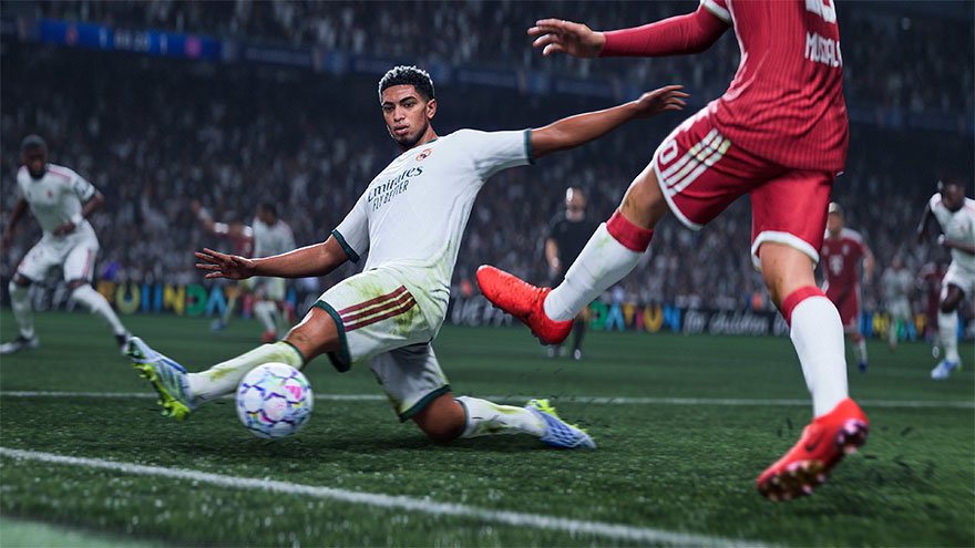Een voetballer in een wit tenue maakt een sliding tackle tijdens een wedstrijd in een vol stadion.