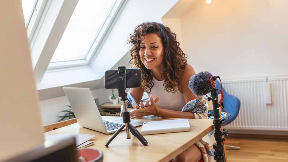 Une table en bois supporte un ordinateur, un téléphone sur un trépied et un micro. Un radiateur blanc est visible en arrière-plan.