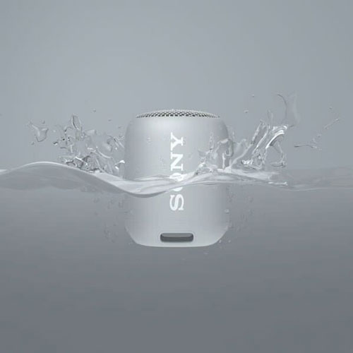 Enceinte Sony blanc dans l'eau. L'eau éclabousse sur les côtés. L'arrière-plan est gris uni.