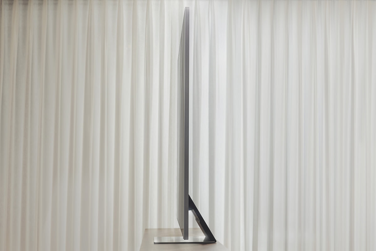 An ultra-thin LG TV stands sideways on a table before light curtains. The design is sleek and very modern.