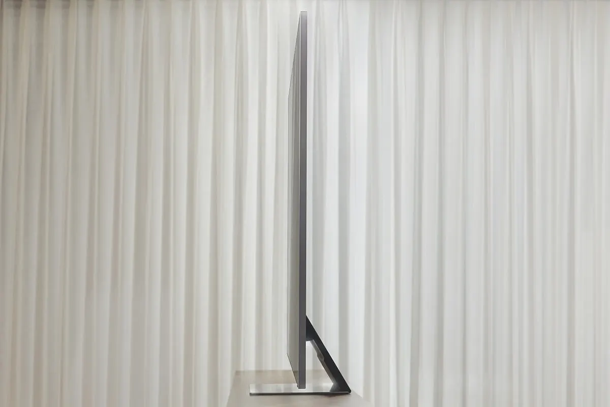 An ultra-thin LG TV stands sideways on a table before light curtains. The design is sleek and very modern.
