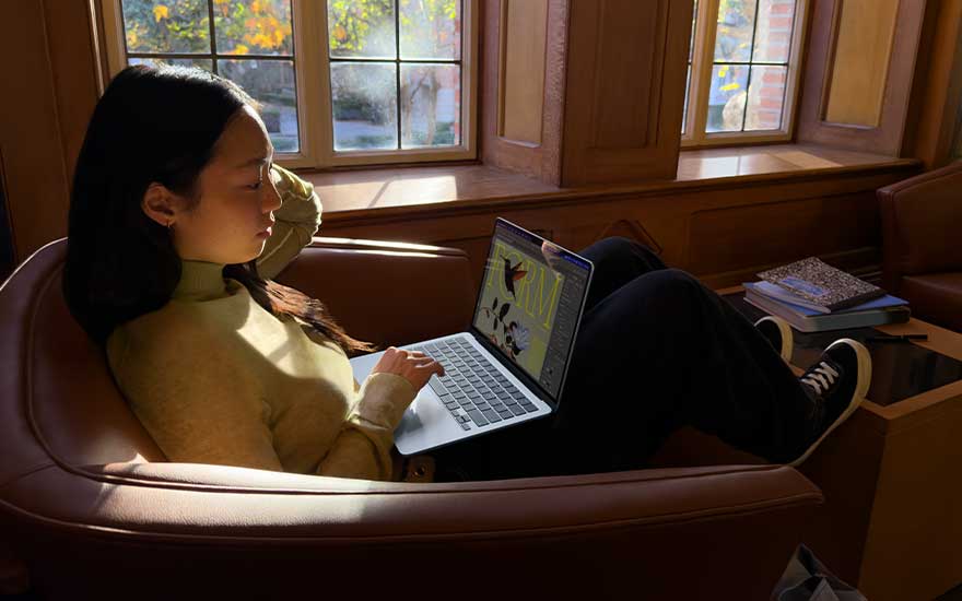 Une personne se détend dans un fauteuil près d’une fenêtre, baignée de soleil, en travaillant sur un ordinateur affichant des visuels créatifs.