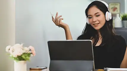 Une tablette sur un bureau avec un vase de fleurs, un casque et une tasse. Une fenêtre est visible en arrière-plan.