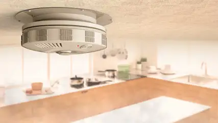 Un détecteur de fumée blanc est fixé au plafond d'une cuisine. Des casseroles sont posées sur le plan de travail.