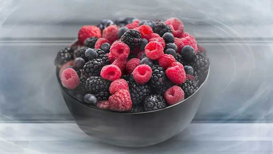 Un bol noir rempli de framboises rouges, de mûres noires et de myrtilles bleues, sur une étagère blanche.