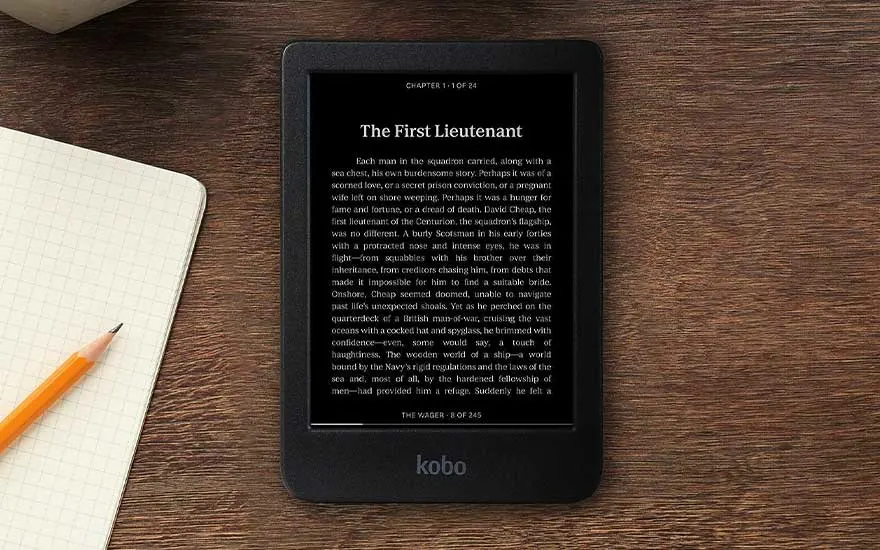 Zwarte Kobo e-reader toont tekst op houten tafel, met notitieboek en oranje potlood ernaast.
