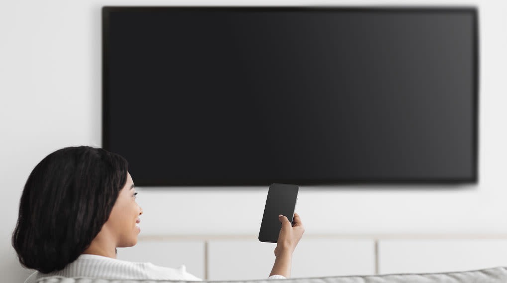 Een zwarte tv hangt aan een witte muur. Een mobiele telefoon wordt in de hand gehouden.