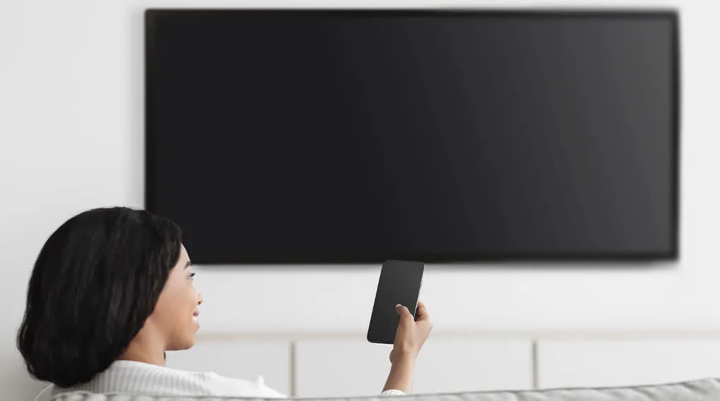 Een zwarte tv hangt aan een witte muur. Een mobiele telefoon wordt in de hand gehouden.