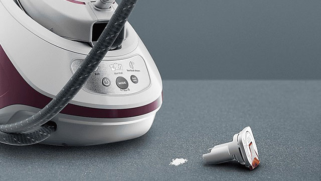 Een stoomstrijkijzer met een slang, een accessoire en wat poeder op een grijze achtergrond.