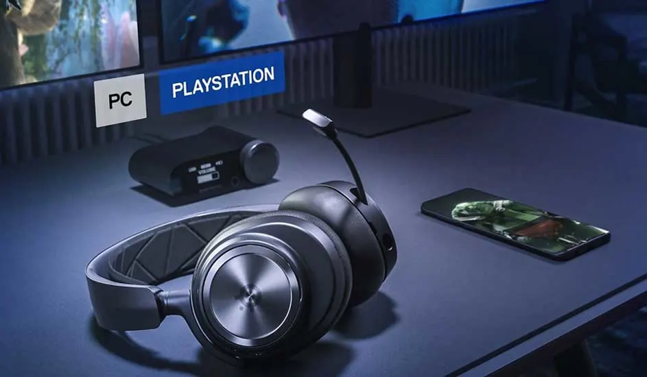 Casque gris avec micro, téléphone et boîtier noir sur table. Écrans avec "PC" et "Playstation" en arrière-plan.
