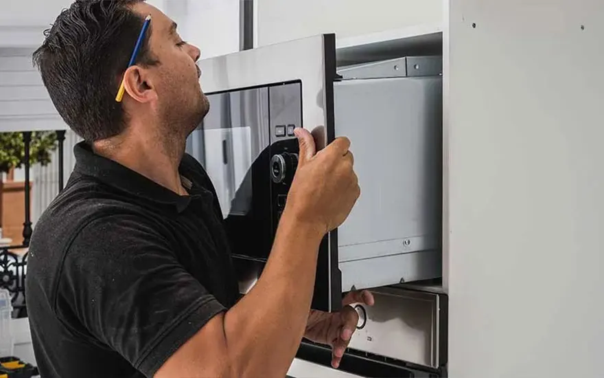 Un homme installe un four à micro-ondes argenté dans une armoire de cuisine blanche.
