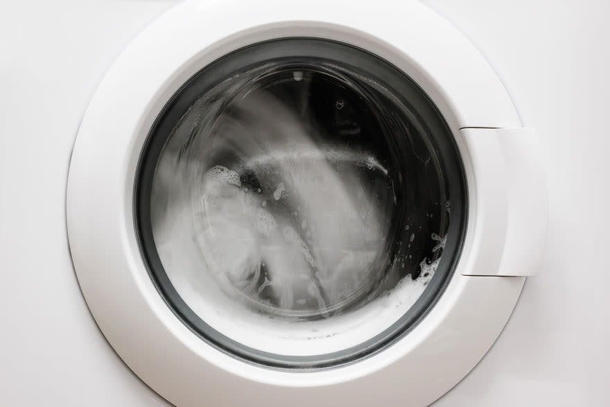 Vue rapprochée d'un lave-linge blanc en marche, avec du linge et de l'eau visible à travers le hublot.