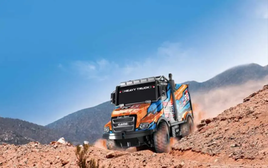 Un camion de rallye aux couleurs vives fonce sur une piste désertique poussiéreuse, grimpant une colline rocheuse devant les montagnes.