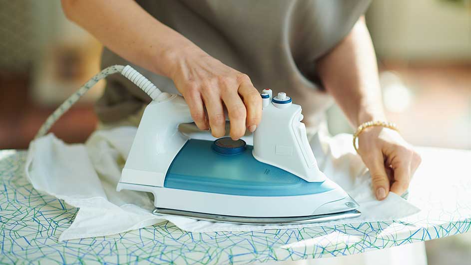 Een blauw-wit strijkijzer op een strijkplank met patroon, strijkend een wit kledingstuk.