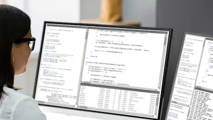 Twee computerschermen tonen programmeercode tegen een vage achtergrond. De code is wit met gekleurde accenten.