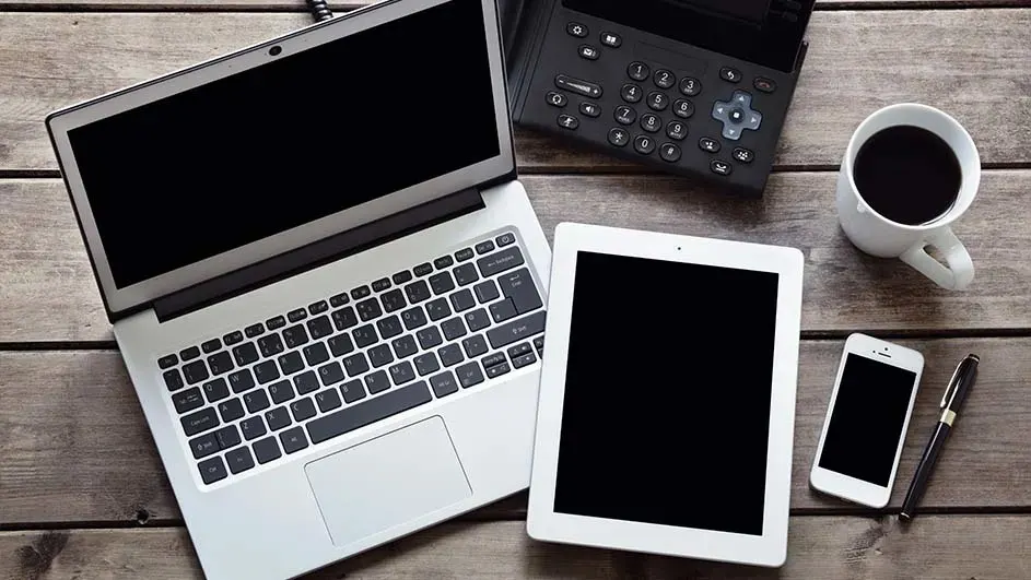 Sur une table en bois, un ordinateur portable ouvert, une tablette, un téléphone, un stylo, une tasse de café et une calculatrice.