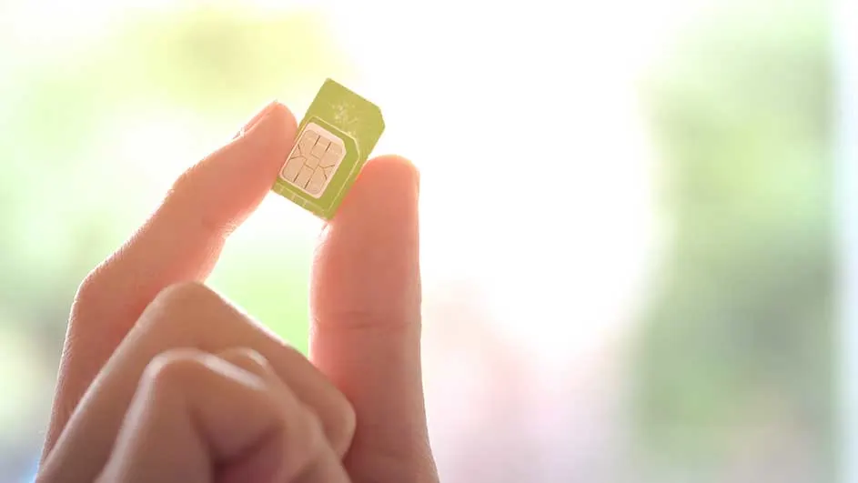 Een hand houdt een groene simkaart vast tegen een vage achtergrond van groen en wit.