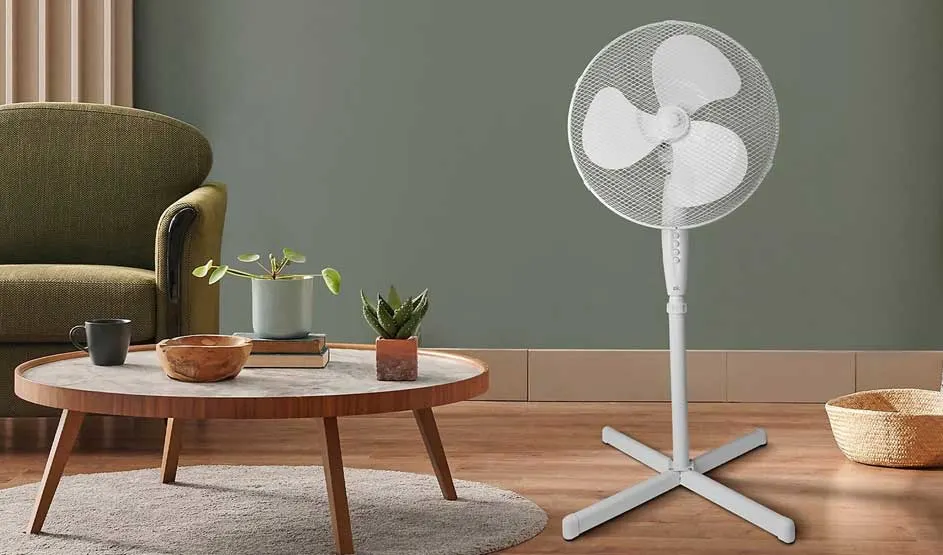 A white pedestal fan with three blades and a grid cover stands against a plain background, simple and functional look.