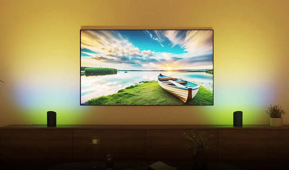 Une grande télévision montre une barque au bord d’une eau calme au coucher du soleil, avec un éclairage d’ambiance coloré.
