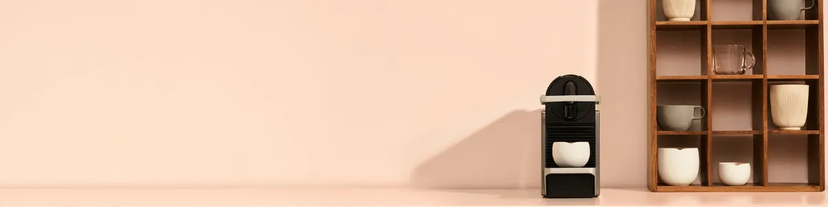 Coin café minimaliste avec une machine compacte et des tasses dans une étagère à cases en bois.
