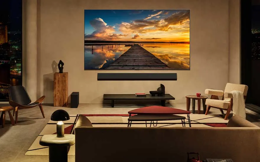 Un salon spacieux décoré avec style accueille un immense téléviseur LG mural, affichant une jetée ensoleillée au coucher du soleil.