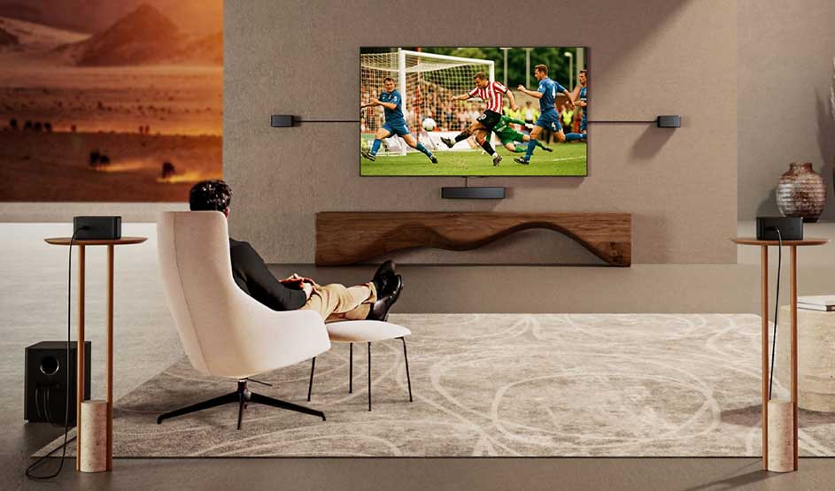 Dans une pièce vaste et élégante, une personne regarde tranquillement une télévision diffusant un match de football, entourée d’enceintes.