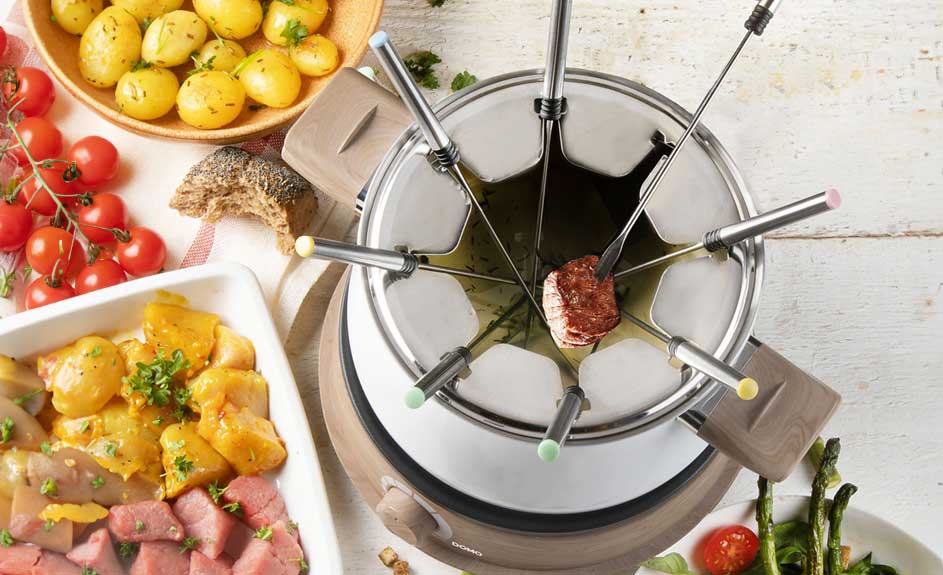 Une fondue avec des pommes de terre, des tomates cerises, des asperges et des morceaux de viande, présentée sur une table en bois.