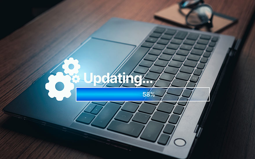 Een laptop voert een update uit, aangegeven door een blauwe voortgangsbalk op 58%. Tandwielpictogrammen zijn zichtbaar. Een bril ligt op de achtergrond.