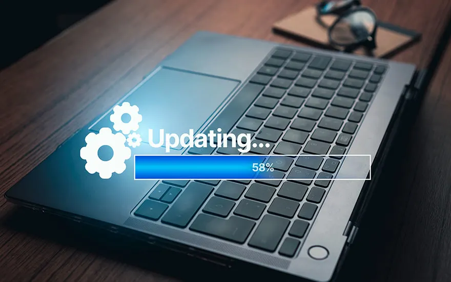 Een laptop voert een update uit, aangegeven door een blauwe voortgangsbalk op 58%. Tandwielpictogrammen zijn zichtbaar. Een bril ligt op de achtergrond.