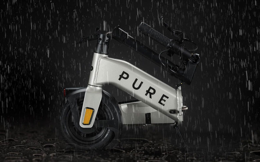 Folded Pure e scooter stands upright in heavy rain, water drops bouncing off its compact, weather resistant frame.
