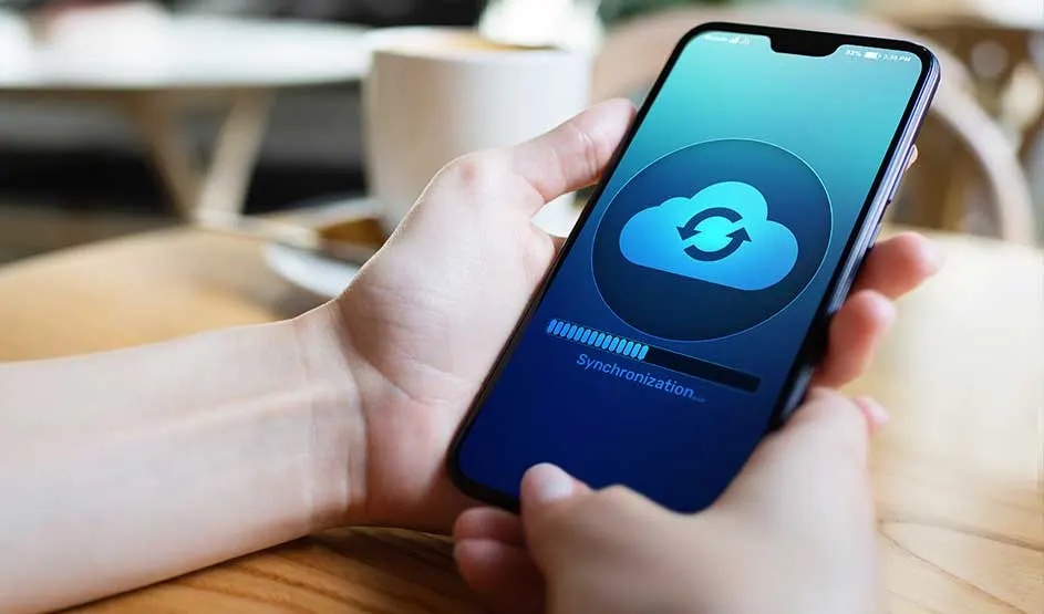 Iemand houdt een smartphone vast waarop een synchronisatie-icoon op het scherm zichtbaar is.