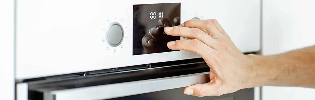 Close-up of a white oven with a hand adjusting the timer, which reads '00:18'. The oven door is partially open.